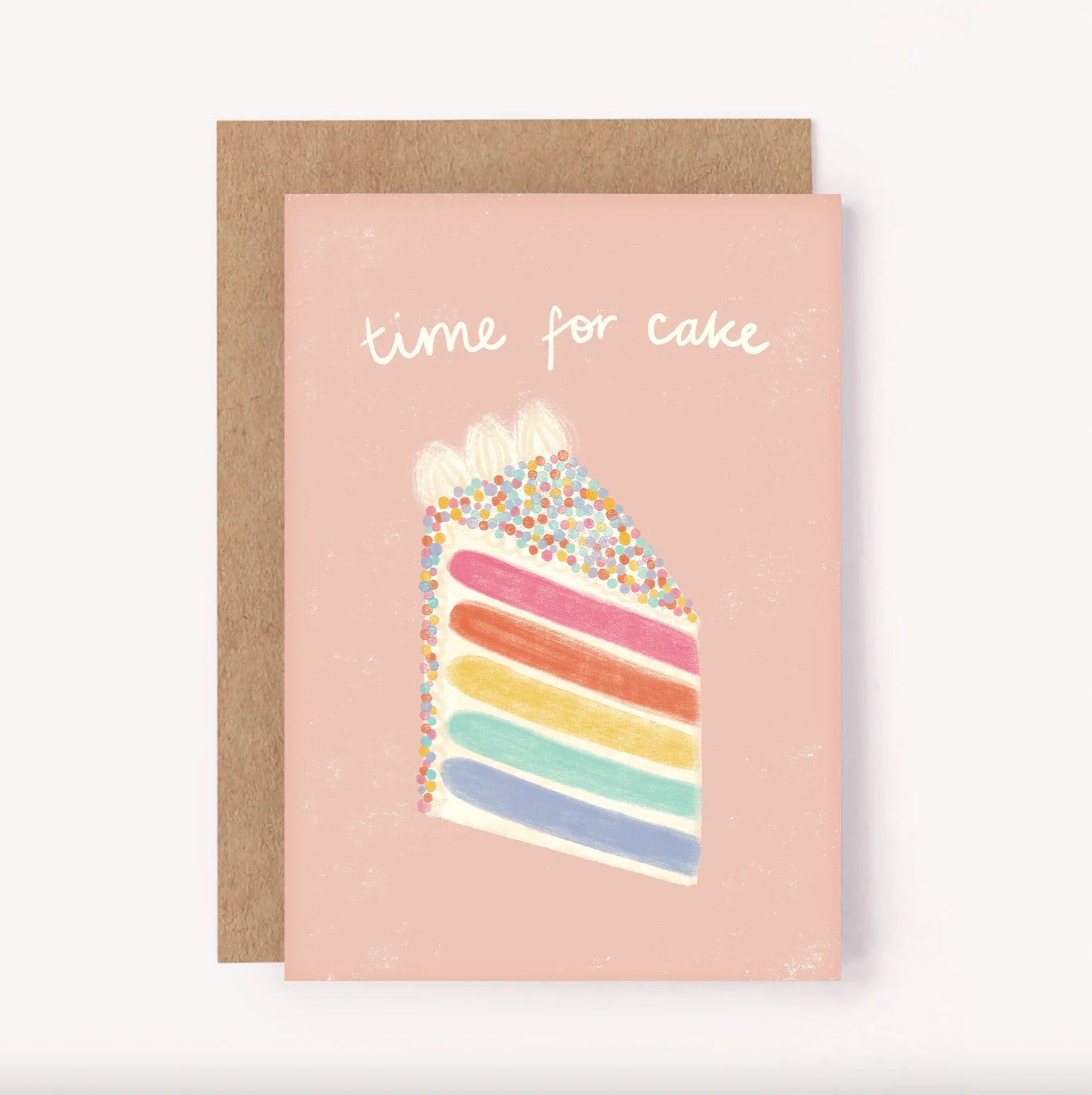 The Birthday Greeting Card "Time For Cake" from LAUREN SISSONS STUDIO features a charming illustration of a slice of rainbow sprinkle cake with white frosting set against a pink background. The phrase "time for cake" is elegantly written above in white cursive text, and the card comes with a brown envelope made from recycled paper.