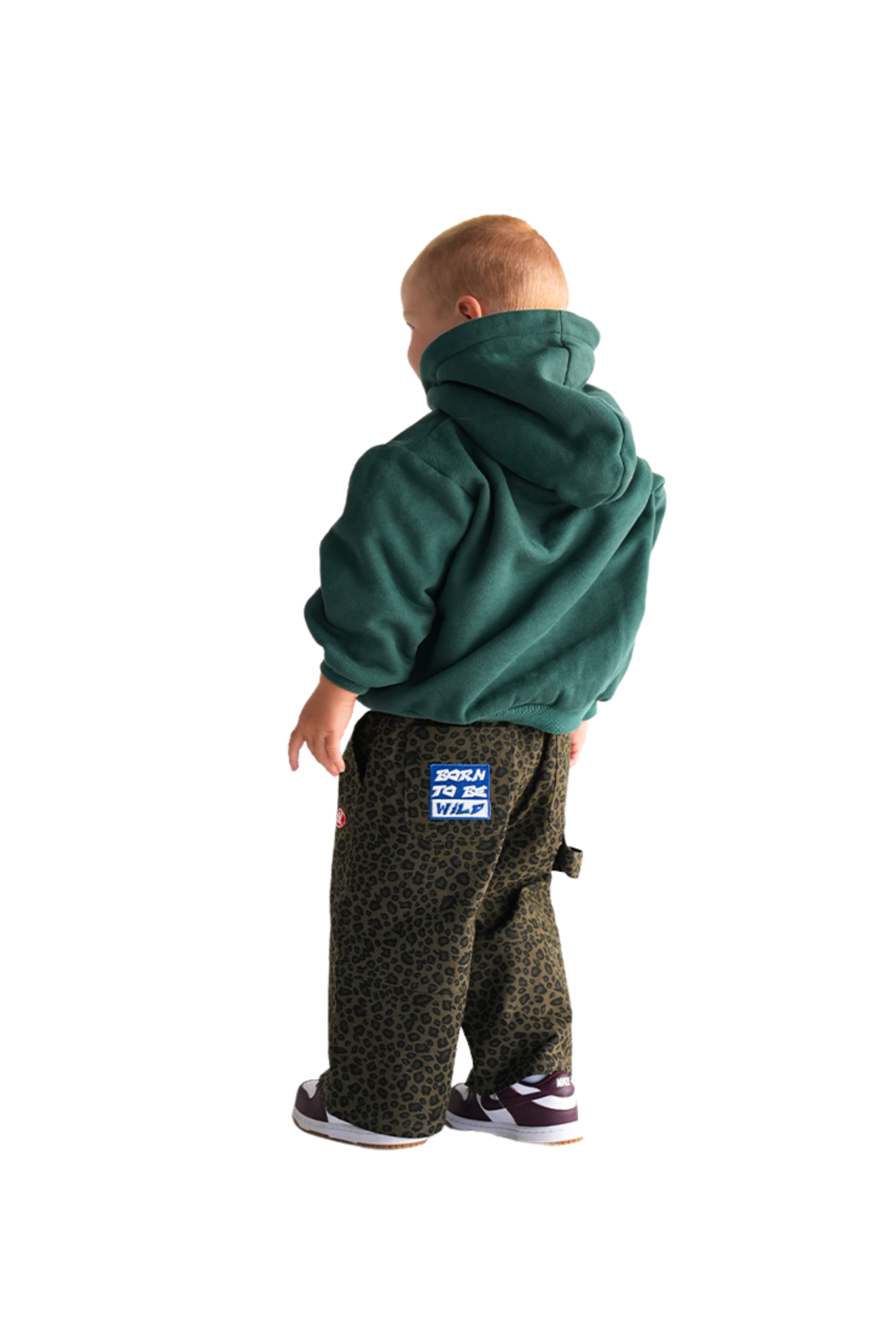 A child turns away, wearing a green hoodie and Franco's Dad ~ PRE-ORDER Leopard Cargos from FRANCO'S DAD. Their short hair pairs well with the pants' stretch waistband, all set against a simple white background.