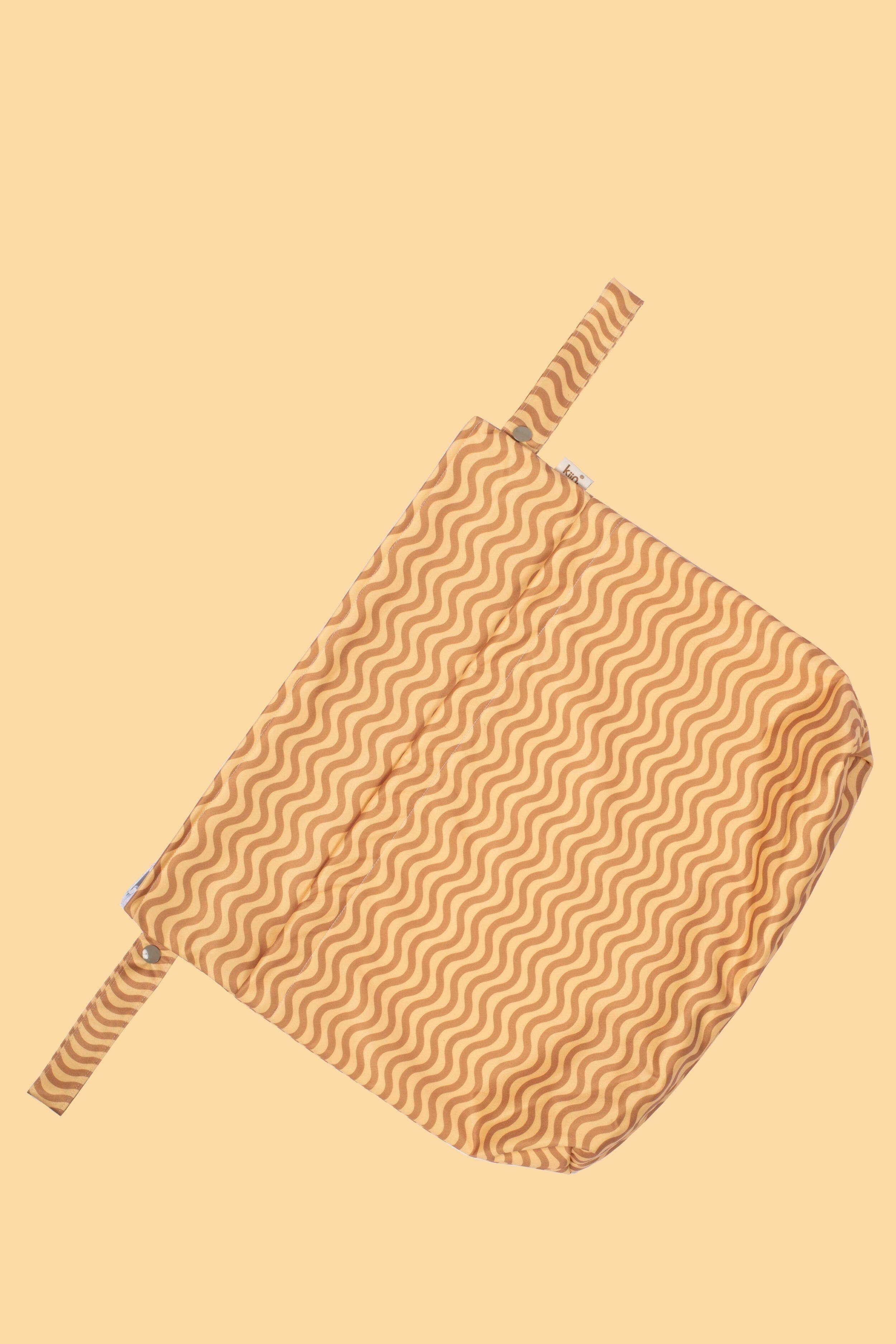 The KIIN BABY Reusable Wet Bag Flower Power is an eco-friendly fabric pouch with a wavy line pattern in beige and brown hues. Featuring a zipper closure, it's perfect for storing cloth nappies or as a reusable wet bag, set on a light yellow background.