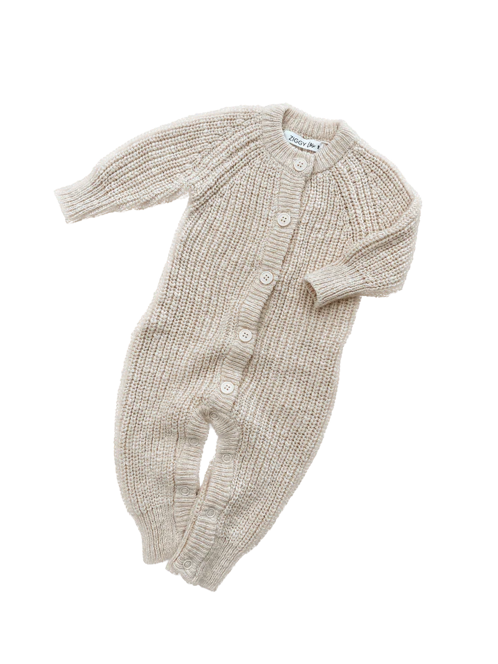 The Classic Knit Romper Honey by ZIGGY LOU is a beige, long-sleeve, ribbed-knit baby jumpsuit with a button-up front closure. This knitted romper has a cozy, textured appearance and features five white buttons running down the center—perfect for a winter outfit.