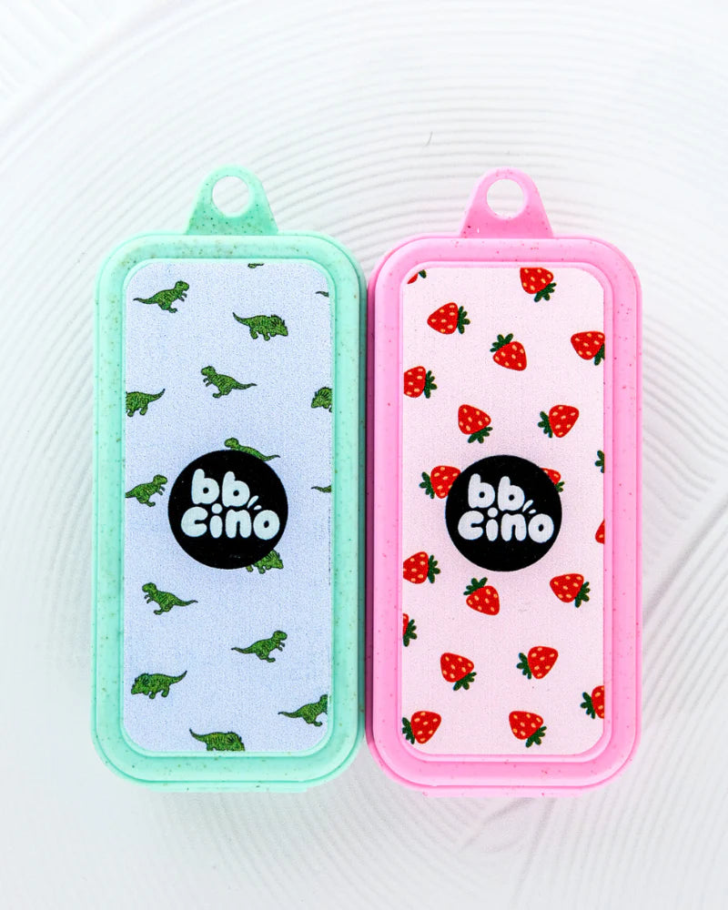 The Replacement Silicone Straw Set by BBCINO features two eco-friendly rectangular keychain accessories with loops, one in mint green adorned with a dinosaur pattern and another in pink decorated with a strawberry pattern. Both are crafted from BPA-free materials and sport a central black circle logo that reads "bb. cino.