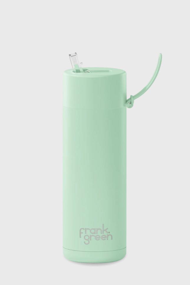 A mint green reusable travel cup with a lid and retractable straw. Made with stainless steel construction, this Frank Green Ceramic Reusable Bottle (595ml - 20oz Straw Lid - Mint Gelato) features a handle attached to the lid and displays the brand name "FRANK GREEN" in gray letters near the bottom. The background is a plain light gray.