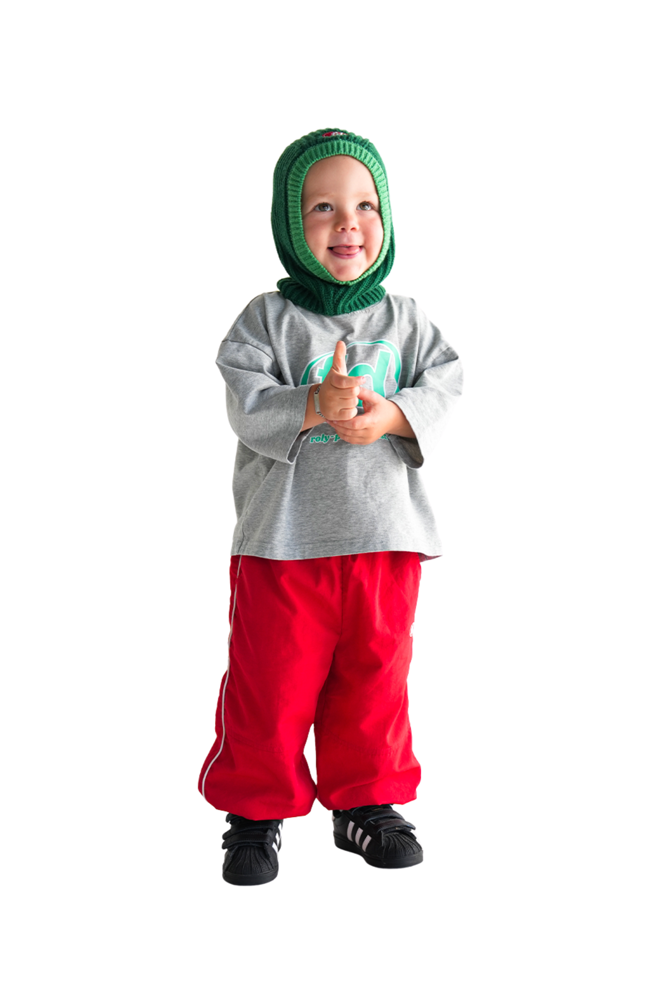 A child beams in a green knit hat, gray long-sleeve shirt, and FRANCO'S DAD Franco's Dad ~ Sports Star Tracks Red pants, hands together on a plain white backdrop that accentuates their playful comfort.