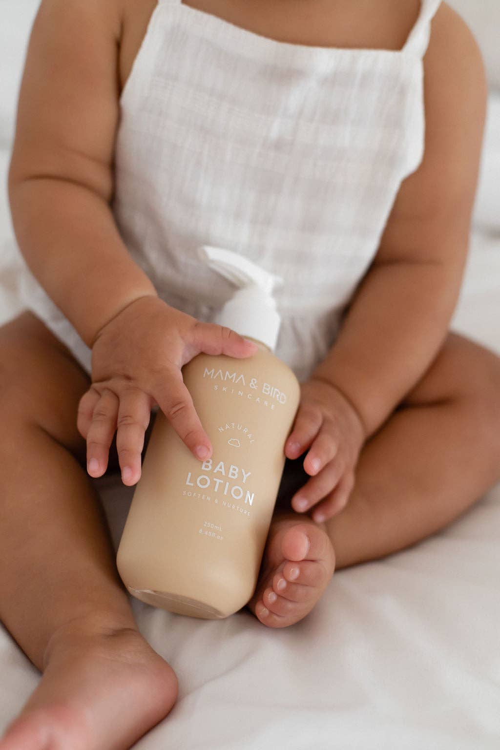 Baby holding a Mama and Bird Baby lotion bottle.