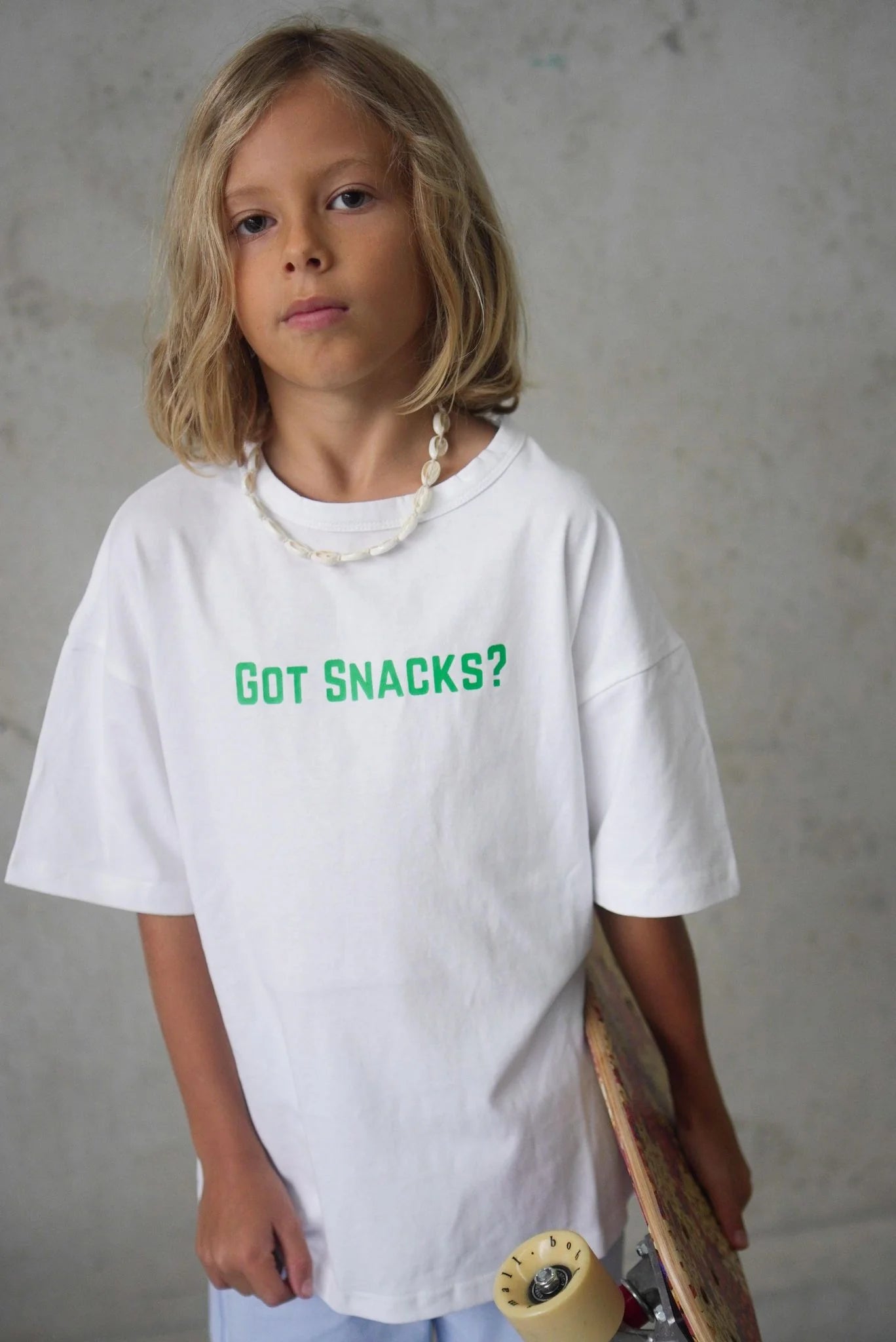 Young boy wearing got snacks tee holding a skate board.