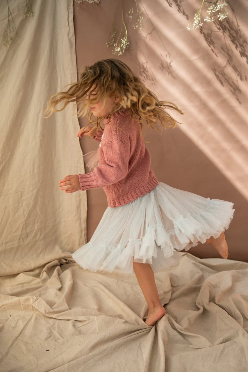 A young girl twirling in her carrie iced lake tutu with brown drapes in the background.