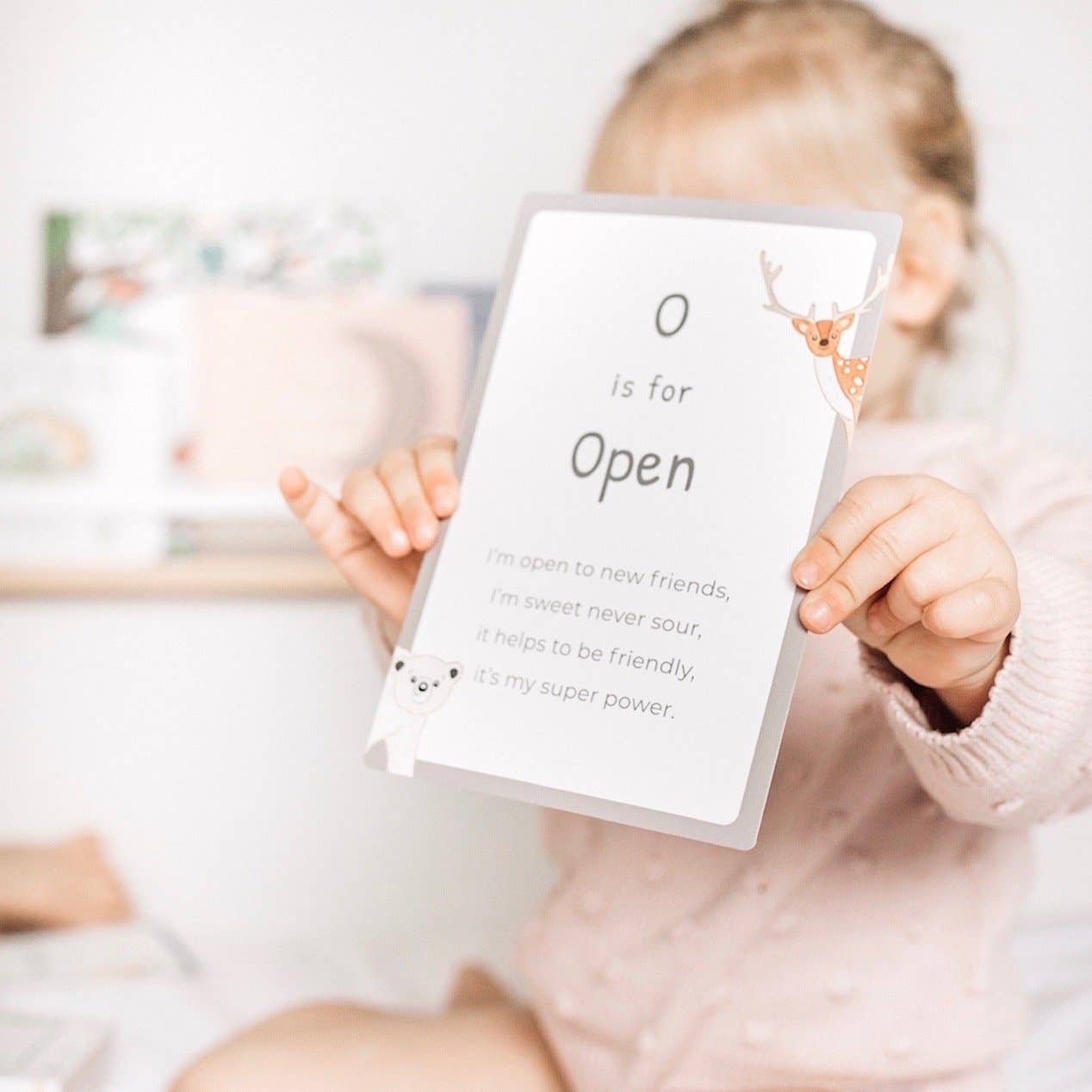 The O letter mindful affirmation card held up by a young girl covering her face.