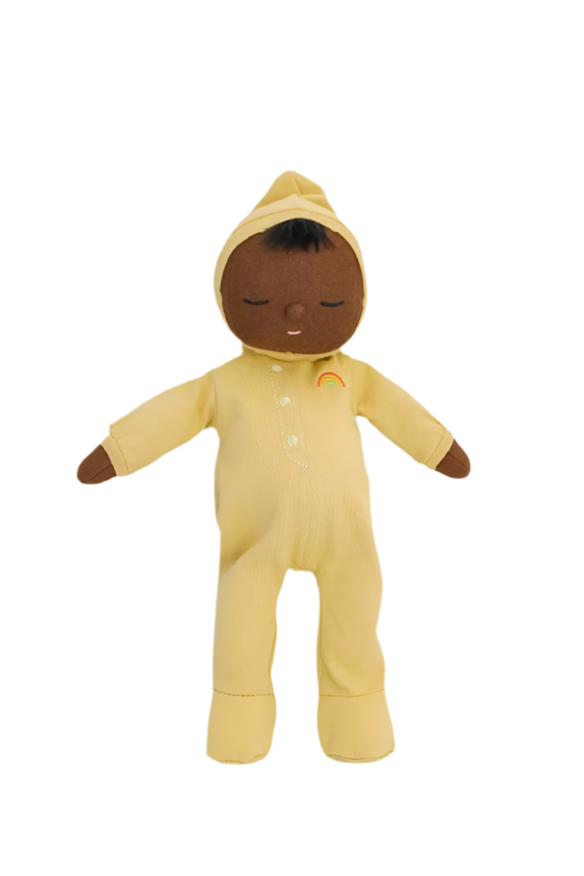 The Dozy Dinkum Mini toy from OLLI ELLA, dressed in a yellow onesie with a hood and featuring an embroidered rainbow on the chest, has a brown face and closed eyes that give it a peaceful expression. This simple and cute doll makes an ideal newborn gift.