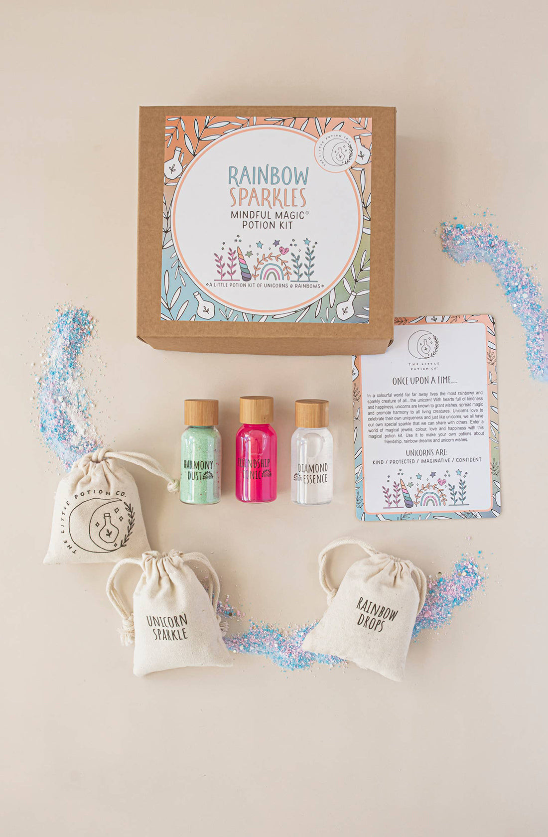 Image shows an open Rainbow Sparkles MINDFUL Potion Kit from THE LITTLE POTION CO. Inside are three small bottles containing green, pink, and transparent liquids, along with three small fabric pouches labeled "Unicorn Sparkle," "Rainbow Drops," and "Lemon Squeeze." Glitter is scattered around, making it perfect for sensory play.