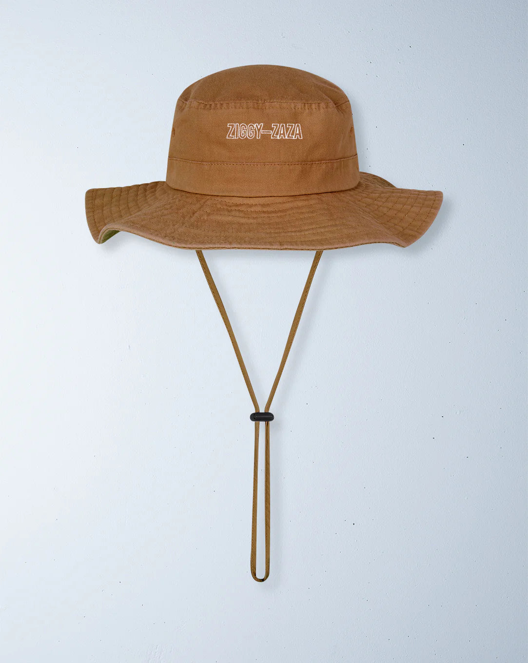 A brown Ziggy Zaza ~ Everyday Scout Hat Otter, made from cotton canvas with an adjustable chin strap, is displayed against a white background. It features "ZIGGY ZAZA" embroidered in white letters on the front.