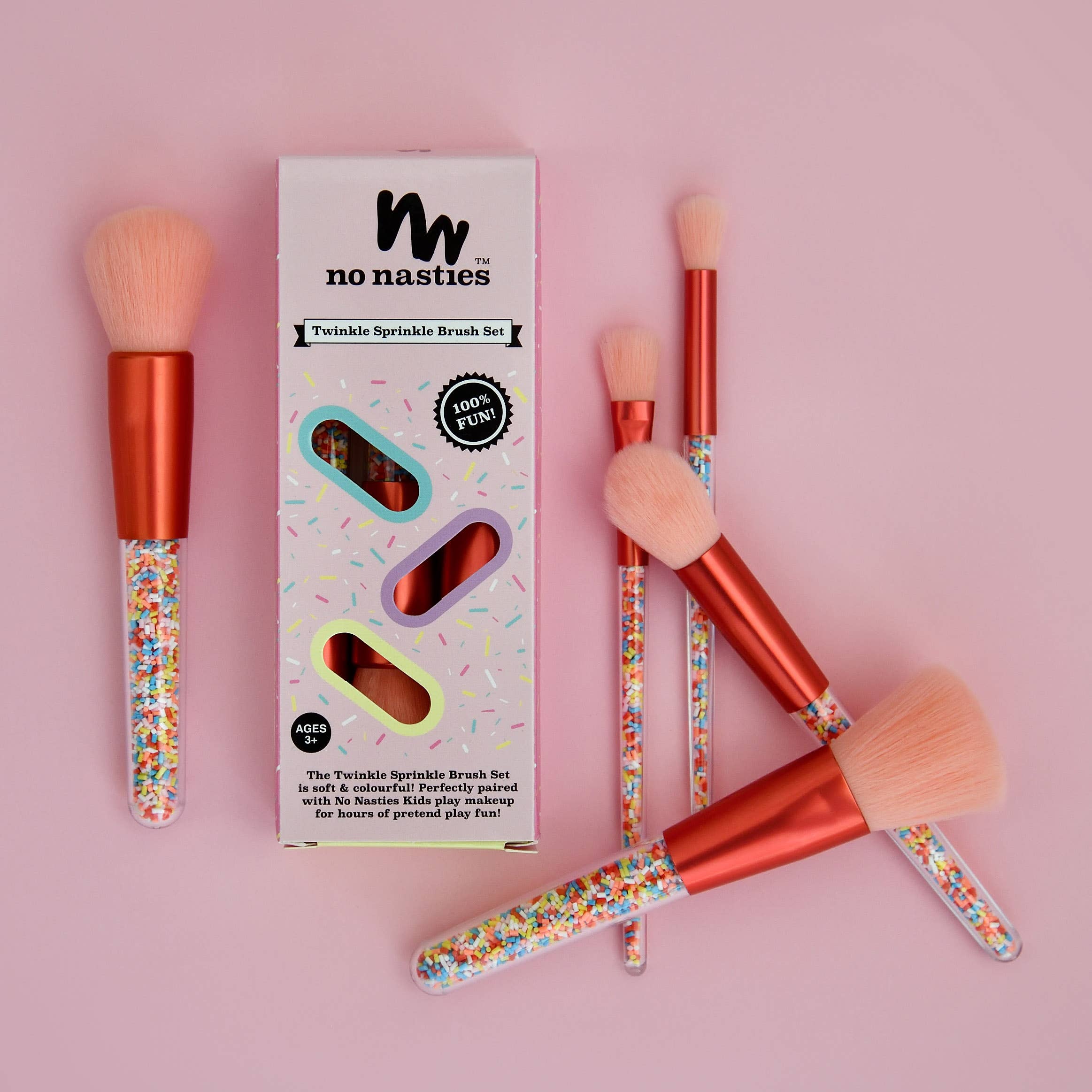 A set of five pink, vegan, and cruelty-free makeup brushes with colorful sprinkle-filled handles is displayed alongside a pink box bearing the "no nasties kids" logo and text that reads "Twinkle Sprinkle Brush Set." The box features fun, colorful designs that match the brush handles.