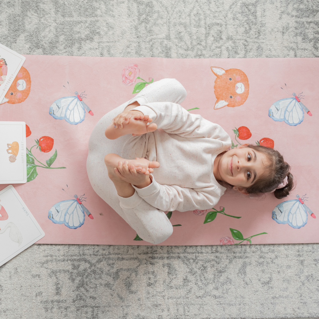 A young girl lying on her back on the sweet themed pink kids yoga mat.