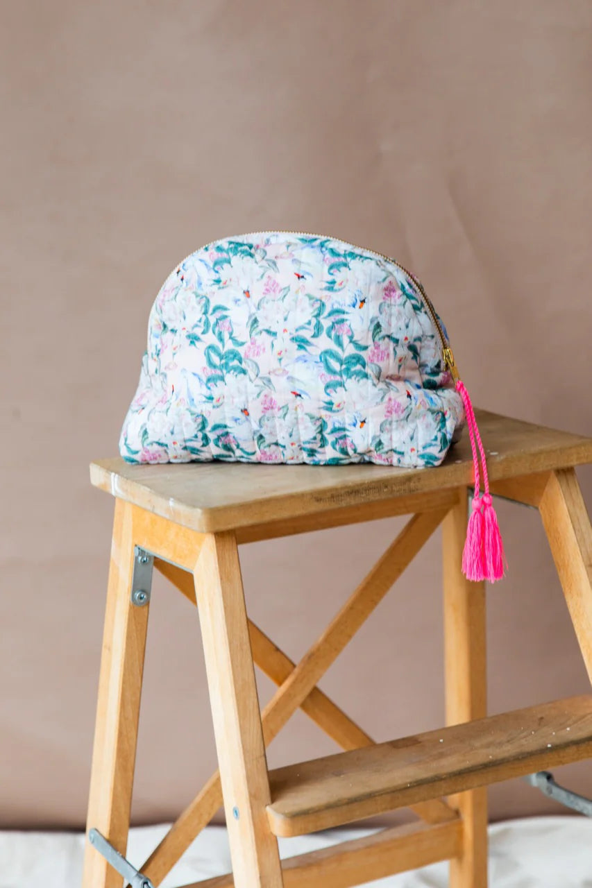 A half moon shaped purse with a floral print design and a pink zip attachment sitting on a wooden step stool.