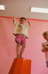 Boy standing on red stool wearing oversized print tee and colourblock boardies