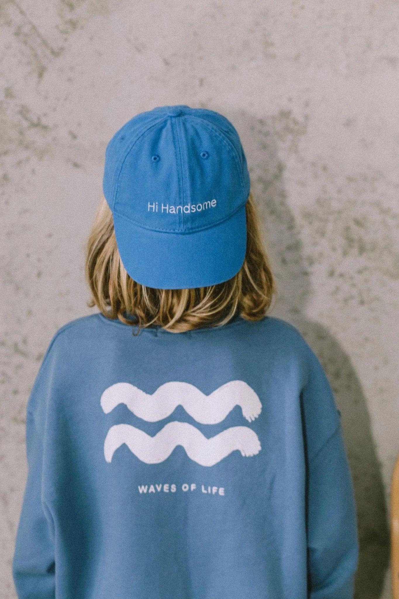 Young boy wearing the wave of life pullover in blue with a blue cap on backwards. 