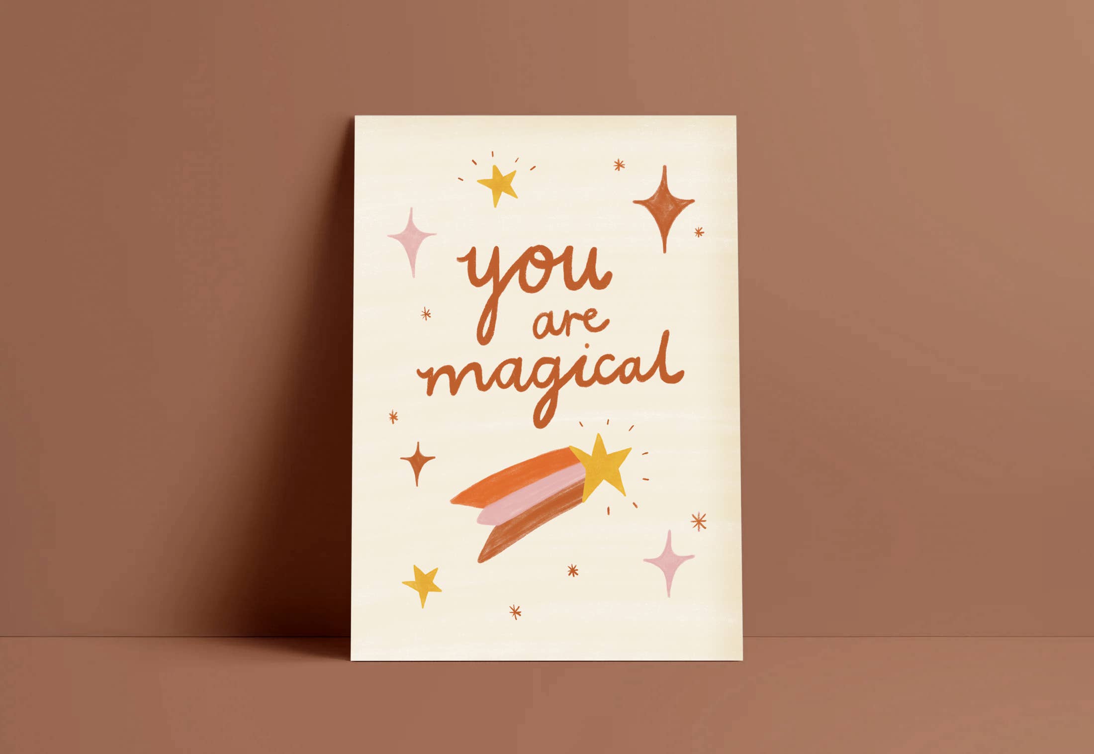 An art print set on a beige background, hand-illustrated type reads "You are Magical" surrounded by tiny sparkles and a shooting star by Laura Sissons Studio.