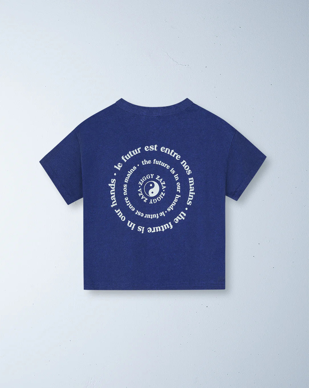 The Ziggy Zaza ~ Love Your Mother Tee in Lapis Blue (Size 7-9) from the brand ZIGGY ZAZA features a relaxed boxy fit, crafted from premium lightweight washed cotton. It showcases white circular text and a central logo with an eye and dotted lines against a light backdrop.