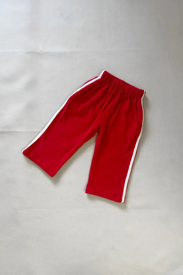 The Darcy Racer Pants Red by TINY TROVE, crafted from premium terry towelling, lay flat on a light surface. These children's pants are red with white stripes on the sides and feature an elastic waistband and a simple design.