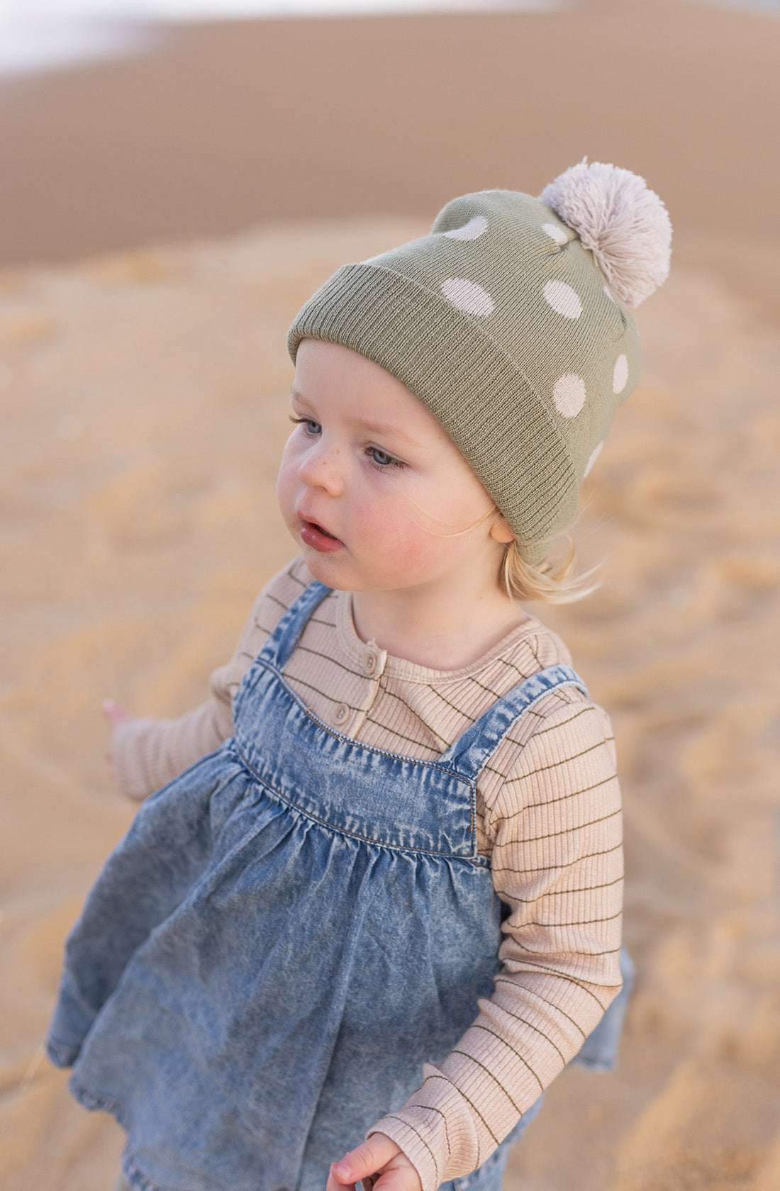 A young girl outside on the beach wearing the raindrops beanie in sage by acorn kids.