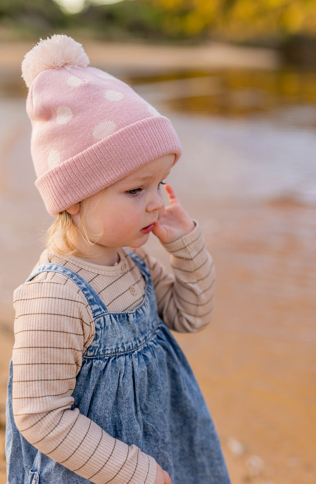 A young girl on the beach wearing the Raindrops Beanie in Dusty Pink by Acorn Kids.