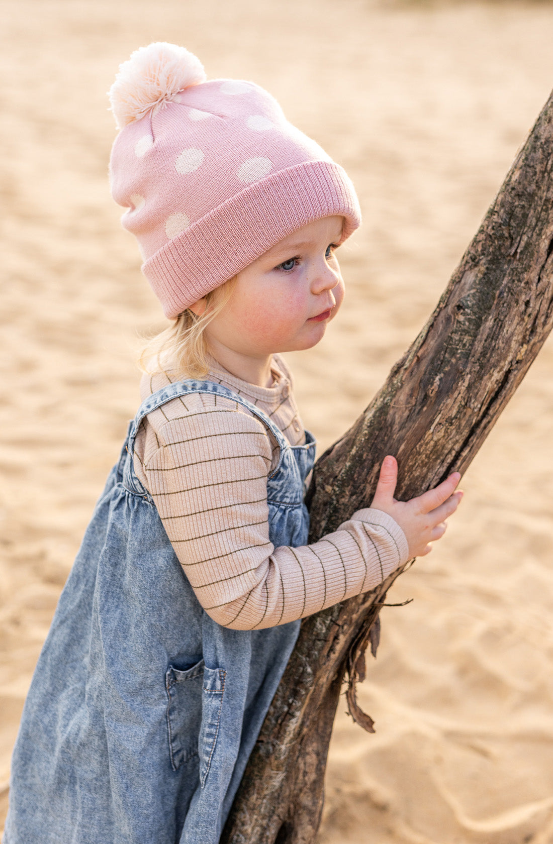 A young girl outside holding a tree branch wearing the raindrops beanie in dusty pink by acorn kids.