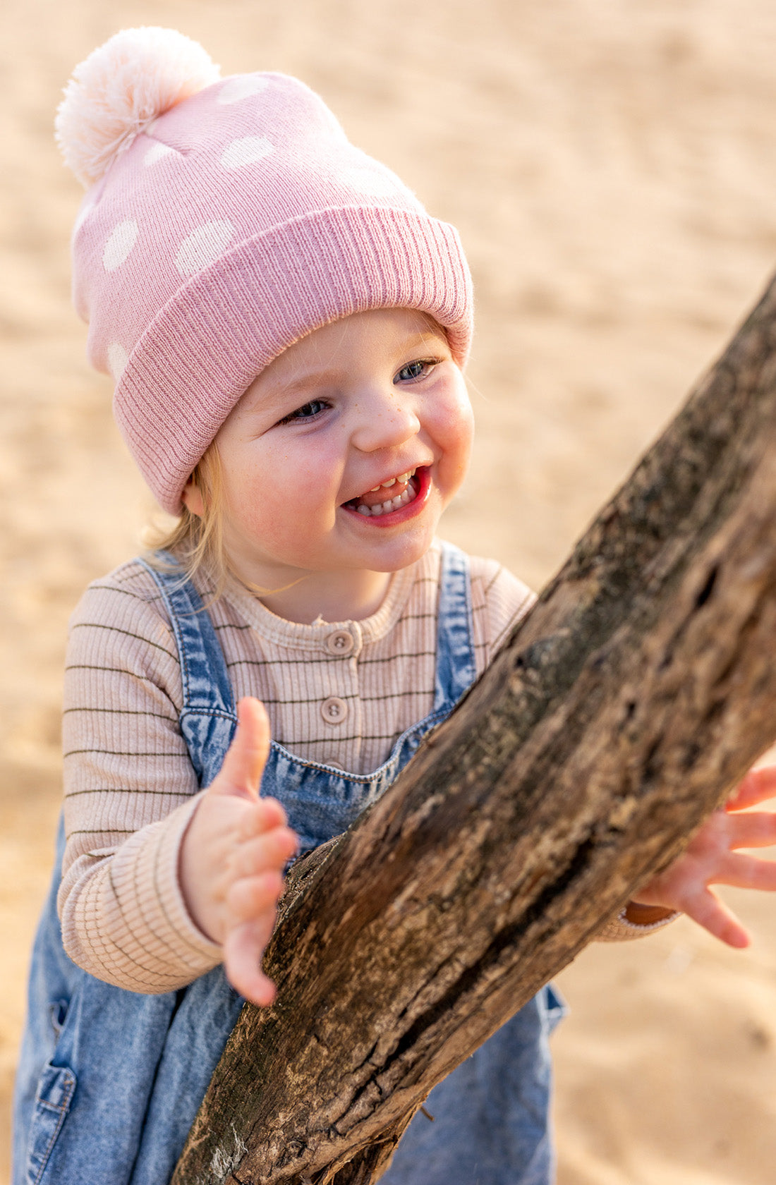 A young girl grabbing a tree branch wearing the raindrops beanie in dusty pink by acorn kids.