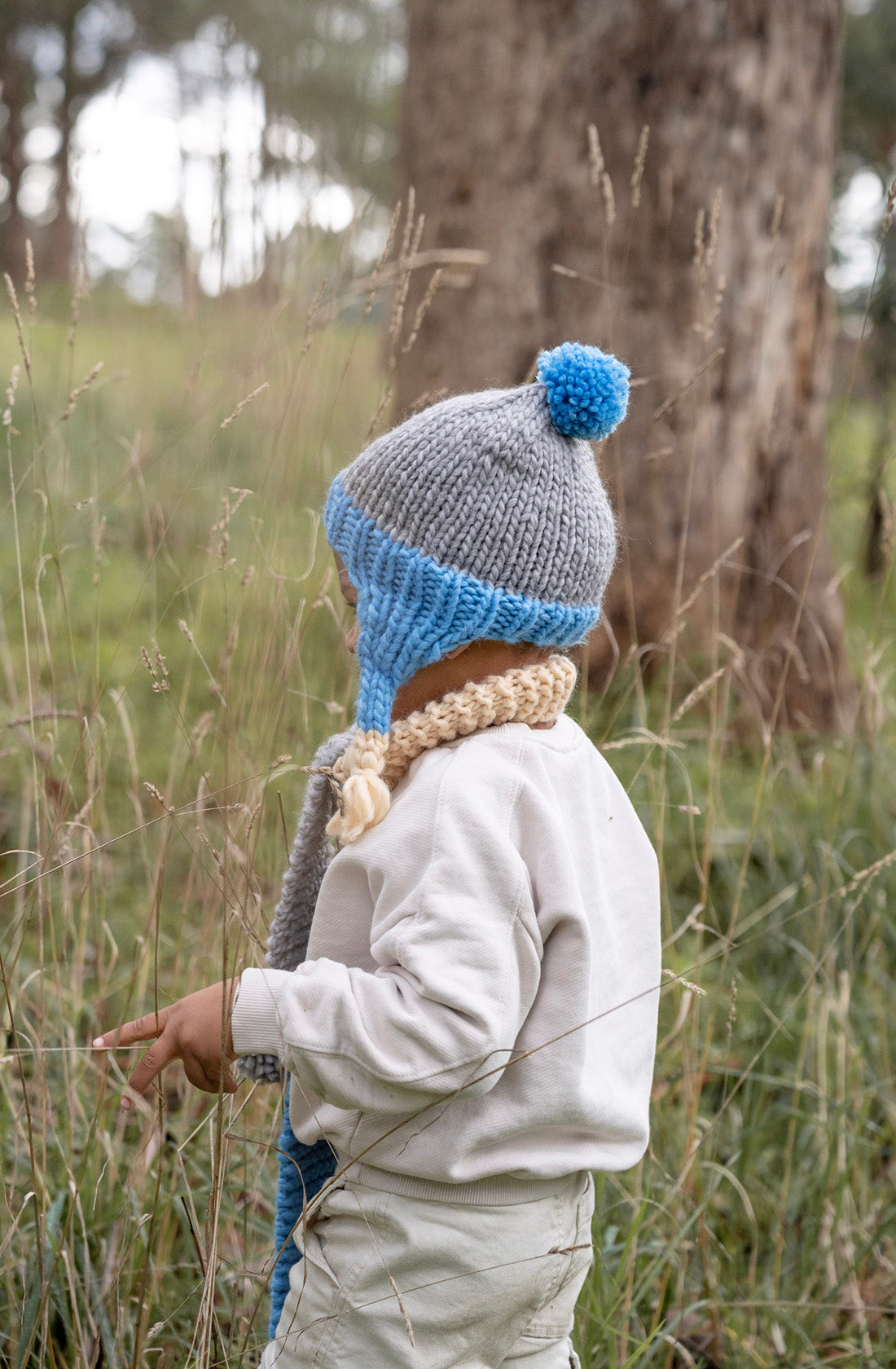 Image from behind of boy wearing blue Acorn Kids beanie in the forest.