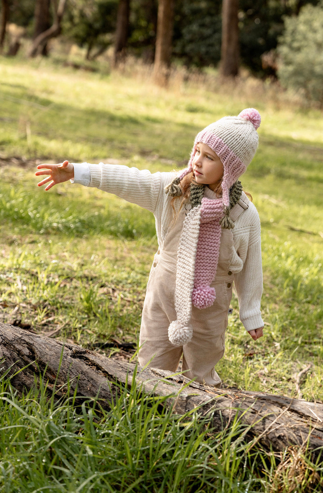 A young girl outside wearing the earth scarf blossom by Acorn Kids with her hand out..