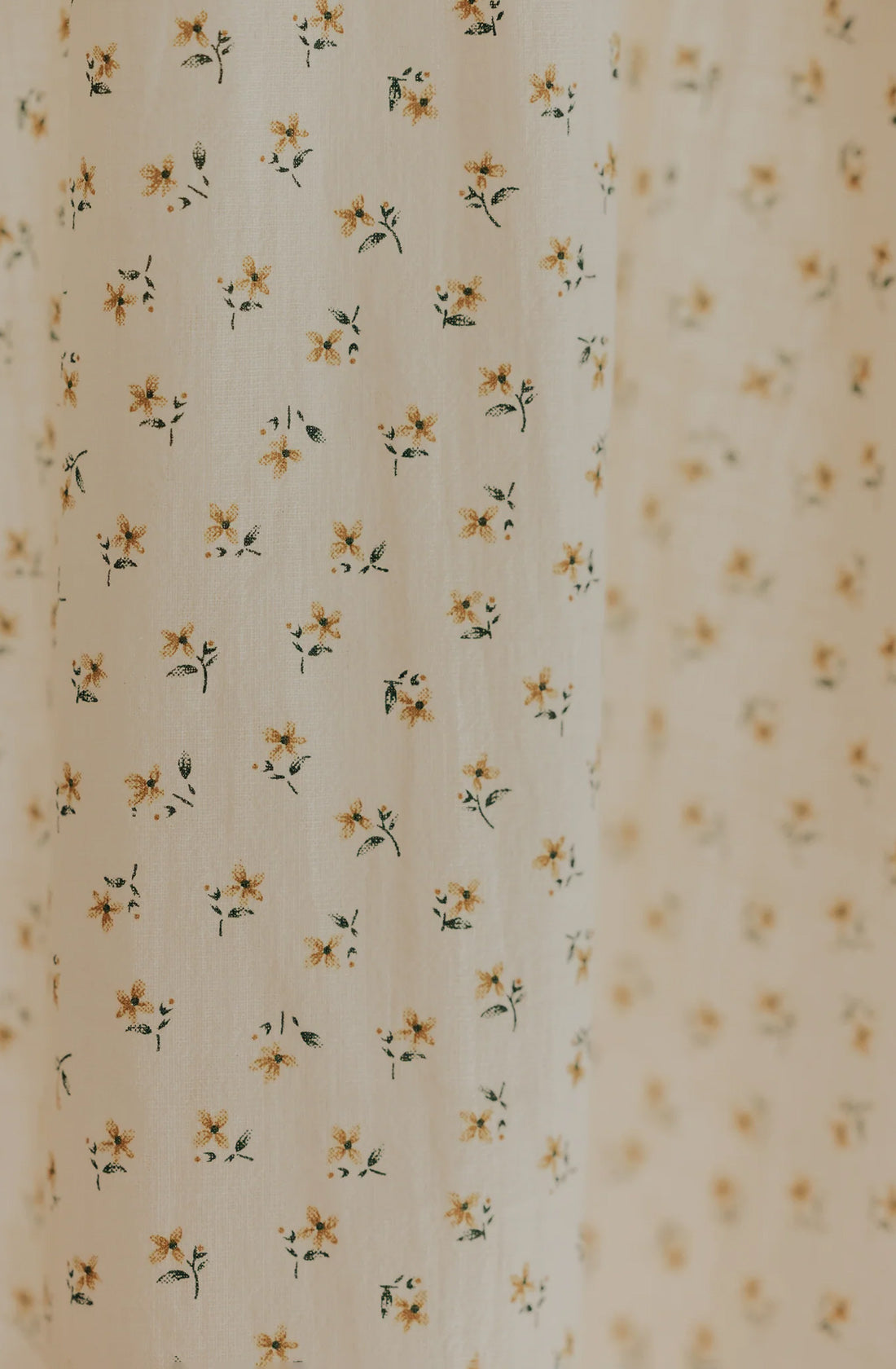 The Farmer's Daughter's Dress from VALENCIA BYRON BAY showcases cream fabric adorned with a charming pattern of small, yellow flowers and green leaves, arranged in an evenly spaced grid-like fashion. This delicate design exudes a vintage feel, while the breathable mid-weight fabric ensures comfort and timeless elegance.