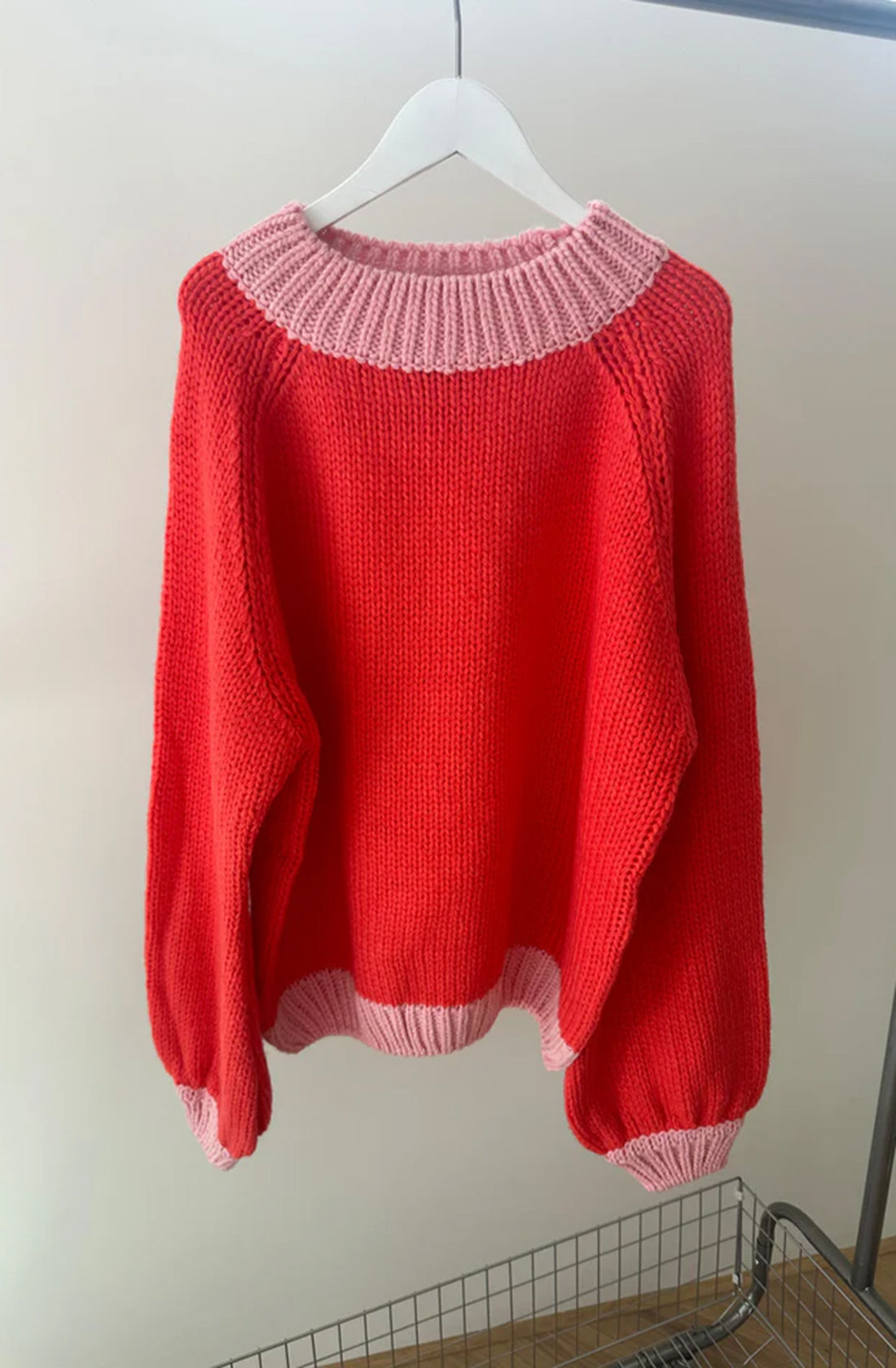 The adult mia contrast knit jumper in red/pink hanging on a coat hanger.