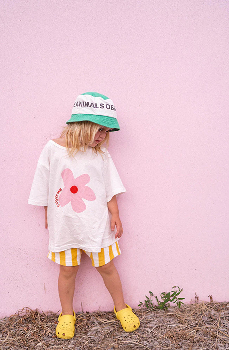 Girl wearing flower print t-shirt and yellow/white striped shorts standing against a pink wall