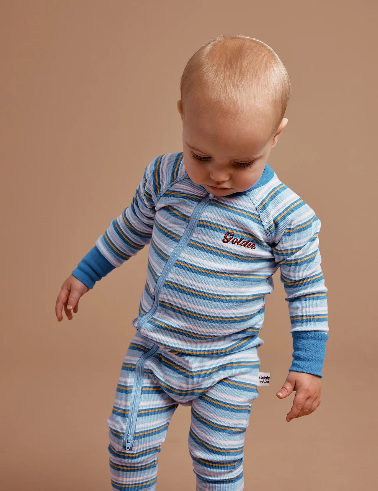 A young toddler wearing the GOLDIE + ACE  Sky Stripe Rib Zipsuit.