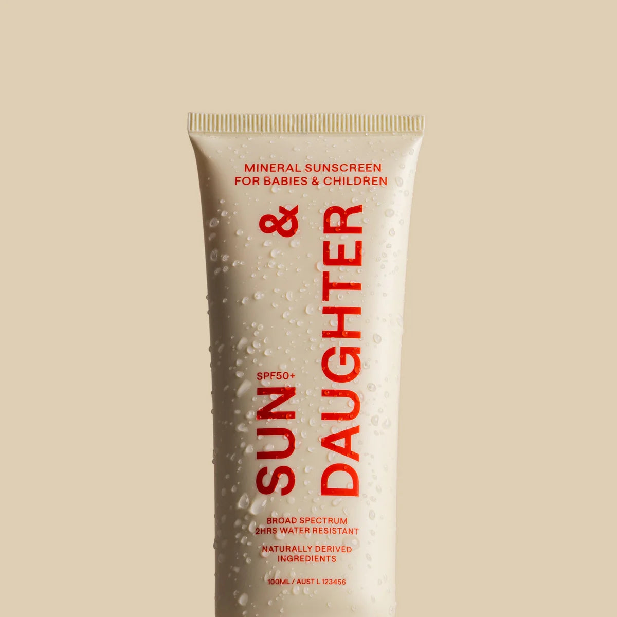 The beige "Sun & Daughter SPF50+ Mineral Sunscreen" tube with red text, labeled as reef-friendly and suitable for babies and children, is shown with water droplets. It offers broad spectrum SPF 50+ protection, promising a gentle experience for little ones.