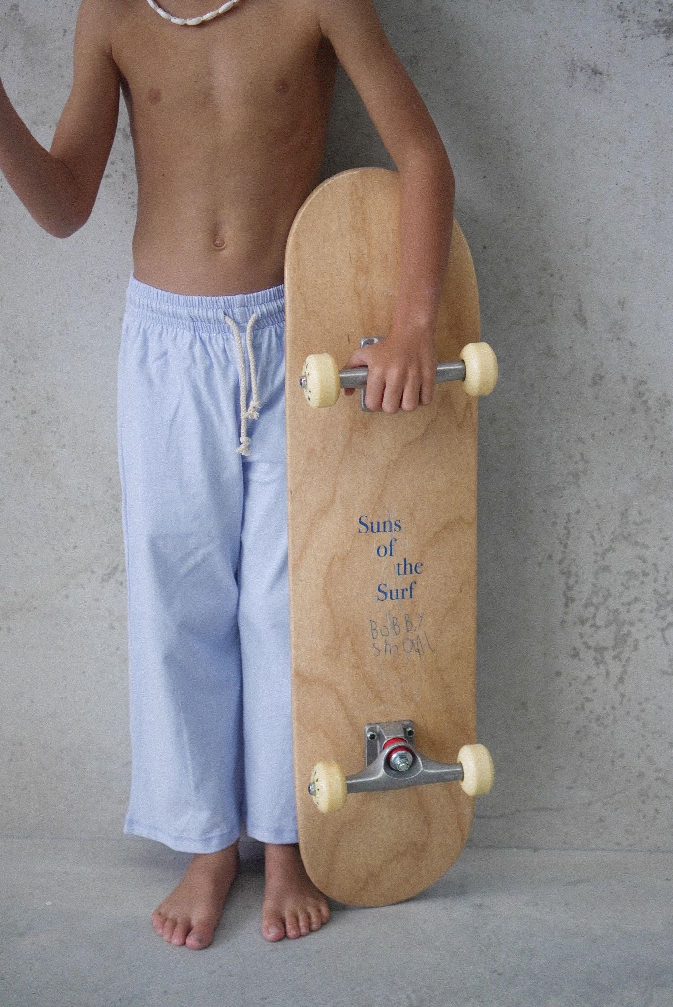 Young boy wearing relaxed beach pant in blue holding a skateboard.