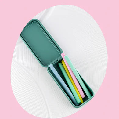 A teal rectangular box from BBCINO's Replacement Silicone Straw Set lies open, revealing five reusable straws made from food-safe silicone in various pastel colors (blue, yellow, green, pink, and light blue) inside. The backdrop is a combination of white and pink abstract shapes. This eco-friendly set adds flair to your daily hydration routine.