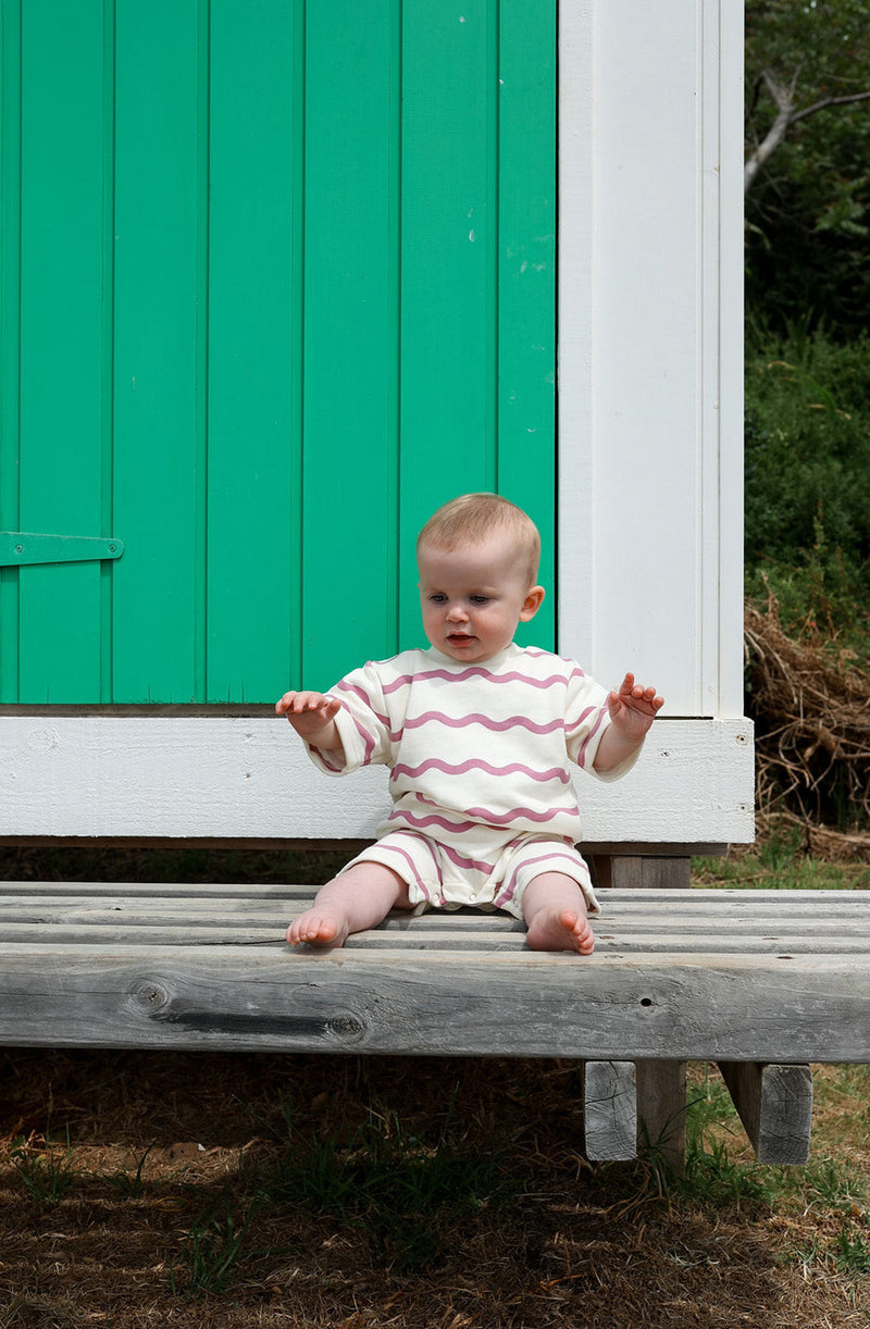 Baby sitting against green and white shed with arms raised
