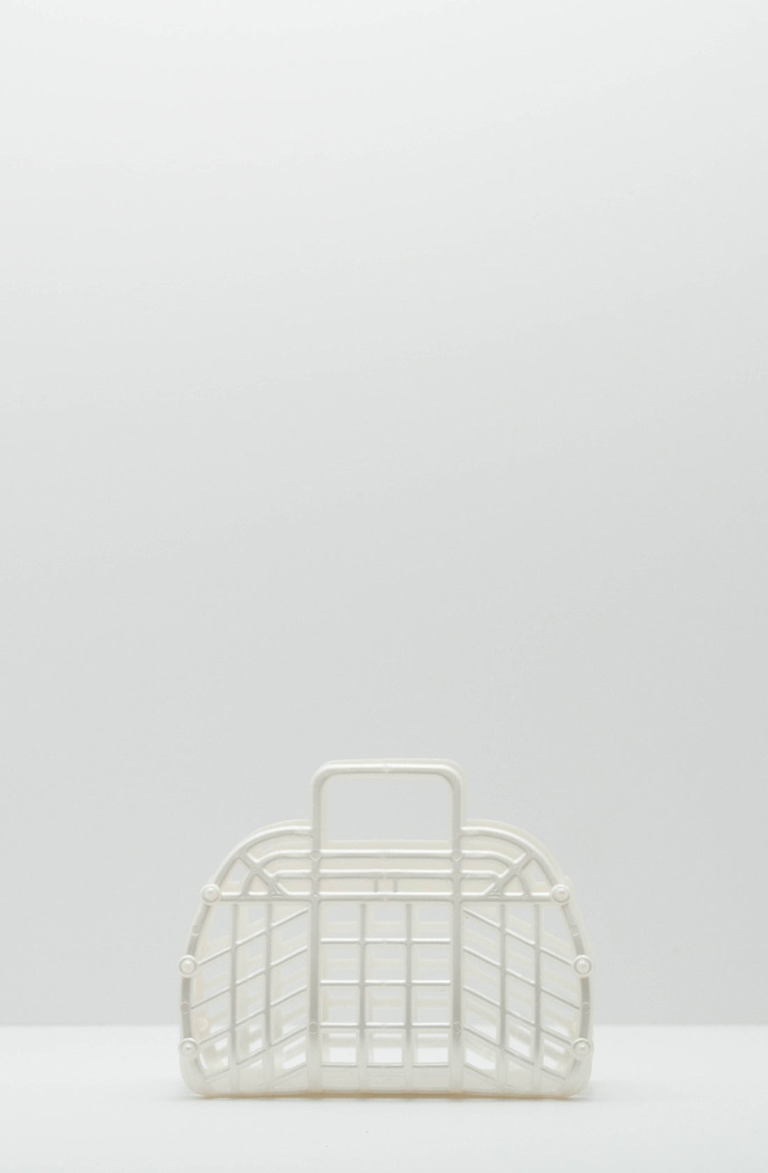 The Mini Retro Jelly Basket Pearl White by BAY KIDS is a white plastic rectangular basket with a curved top, featuring a grid design and a small rectangular handle near the top center. Crafted from recyclable LDPE, this BPA-free retro Jelly Basket is set against a plain, light gray background.