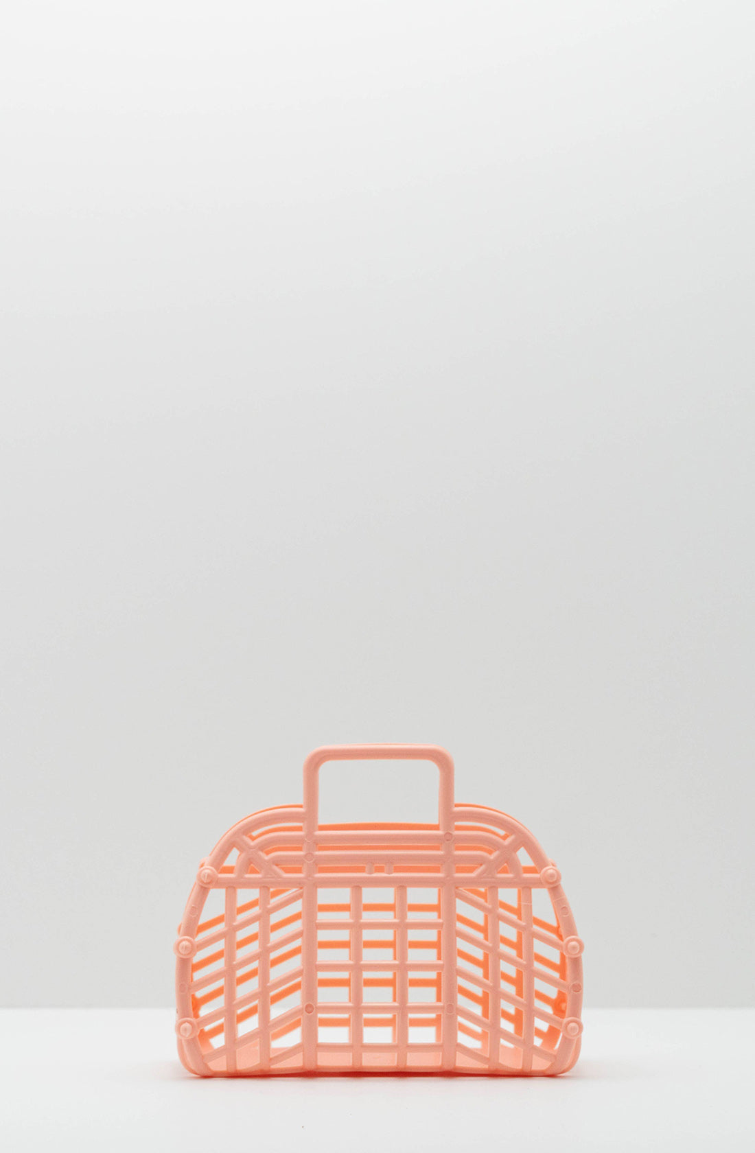 A Mini Retro Jelly Basket Peach by BAY KIDS sits on a white surface against a plain, light grey background. Made from BPA-free plastic in the USA, this small basket features a grid design and a rectangular handle at the top.