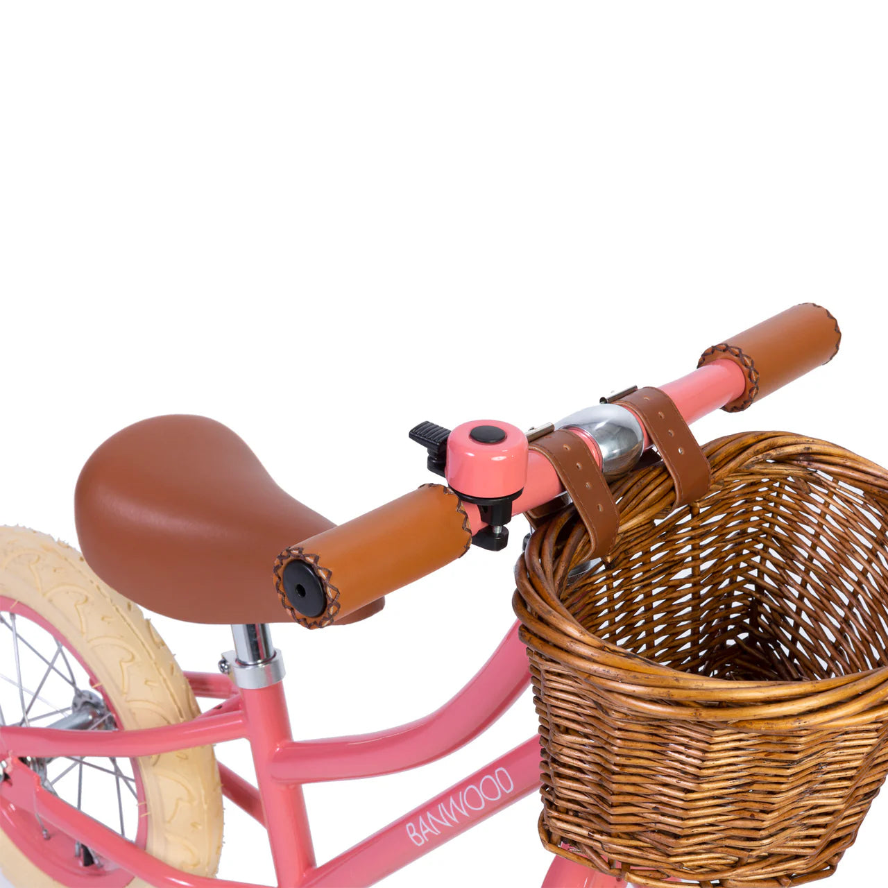 A close up of a coral and black bike bell on the handle of a coral banwood vintage balance bike with a straw basket.