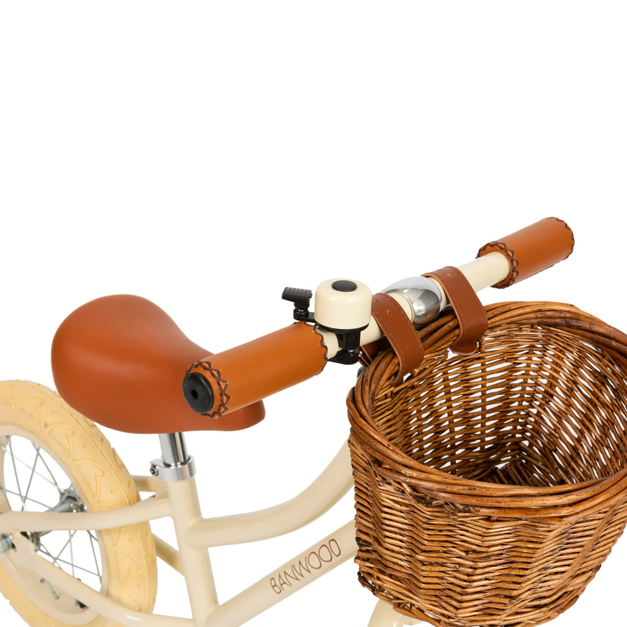 A close up of a cream and black bike bell on the handle of a cream banwood vintage balance bike with a straw basket.