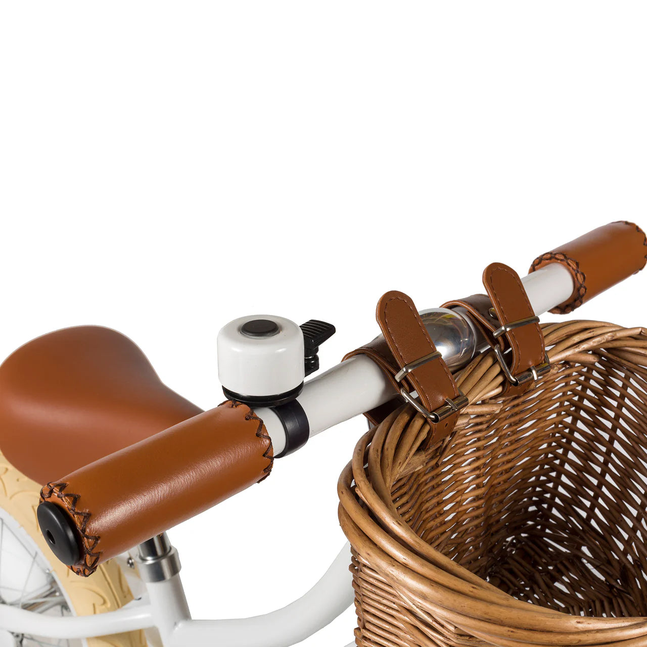 A close up of a white and black bike bell on the handle of a white banwood vintage balance bike with a straw basket.