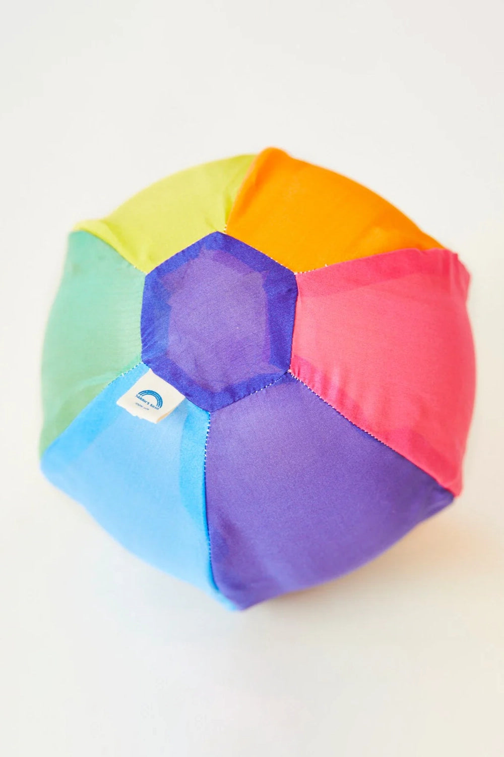 The Rainbow Balloon Ball by SARAH'S SILKS is a lively fabric ball featuring a hexagonal pattern on top with panels in green, yellow, orange, pink, red, purple, and blue. The reusable ball sits gracefully on a white surface.