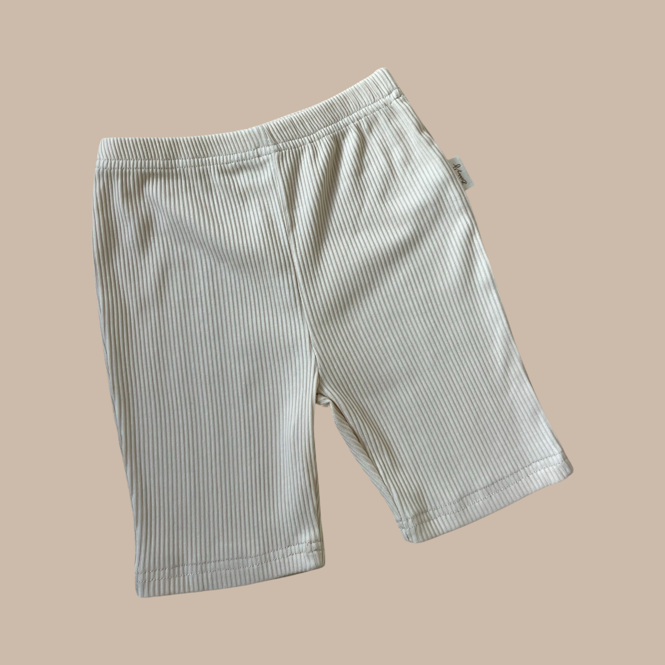 A pair of "Bike Shorts Lemon Sherbet" by BOBBY G BABY WEAR in light beige and white striped ribbed fabric is set against a plain beige background. The shorts boast an elastic waistband and a straightforward design, making them an essential addition to any kid's wardrobe.