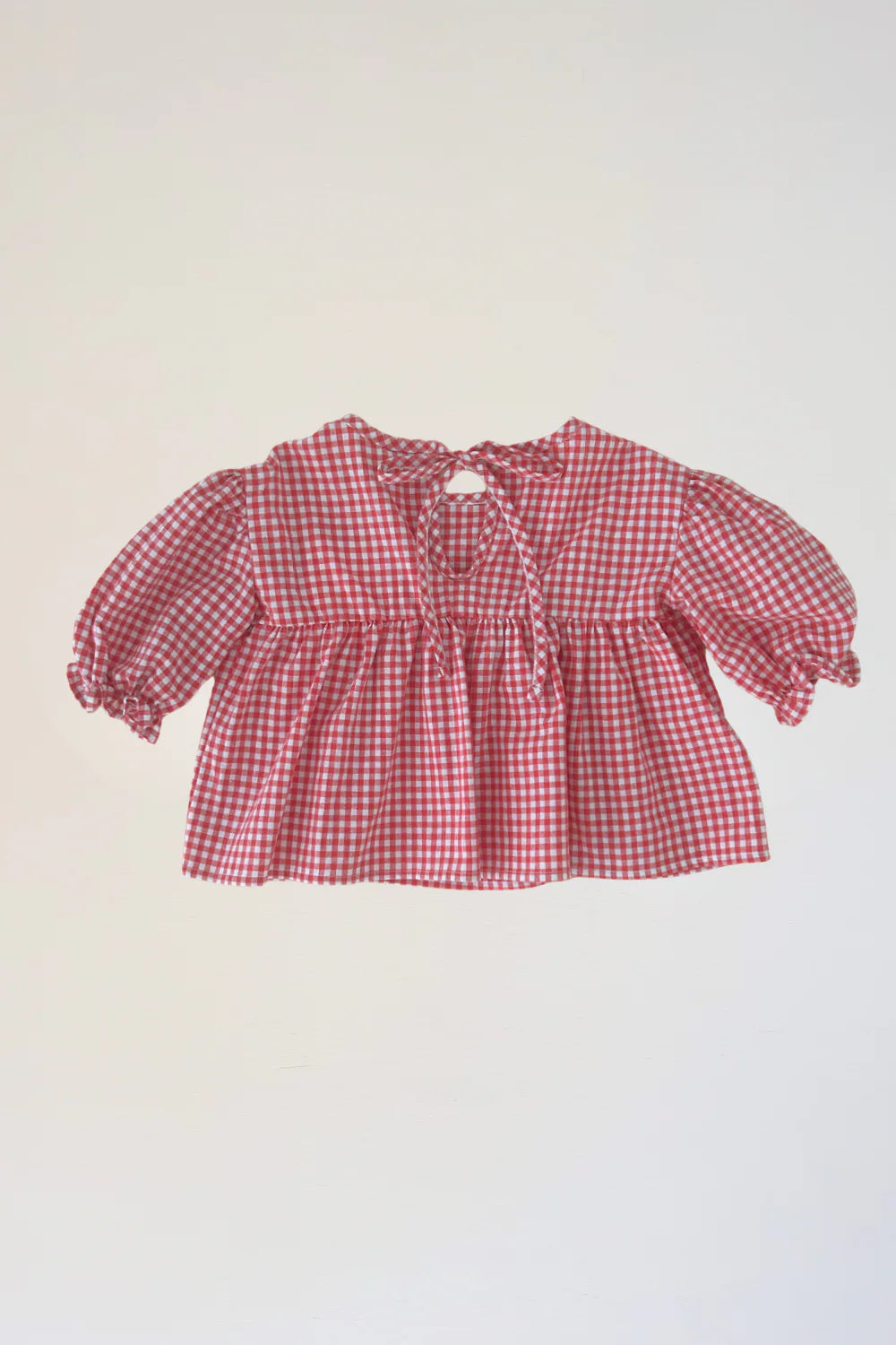 The WORN CURATIONS Gingham Bloom Blouse Chilli is a red and white cotton girls’ puff sleeve top with gathered cuffs and a back neckline bow, shown on a plain light background.