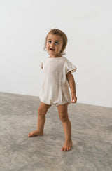 Toddler girl wearing a natural cheesecloth romper with embroidered sleeve detail.