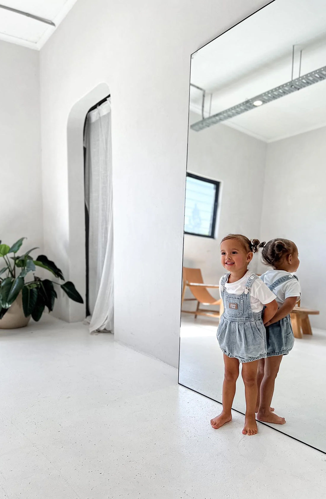 Girls standing in front of large mirror wearing light blue denim romper with white t-shirt underneath