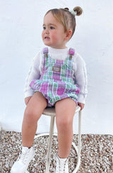 Girl sitting on stool wearing the check romper with a knit underneath