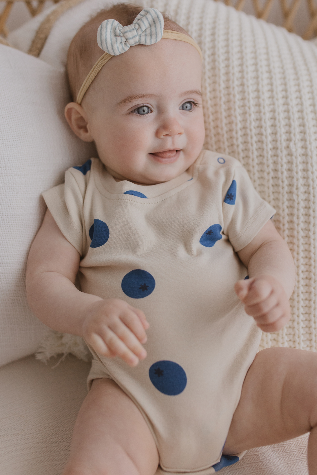 A baby lies on a blanket, snuggled in the Classic Bodysuit Blueberries by SUSUKOSHI, crafted from organic cotton and designed in Australia.