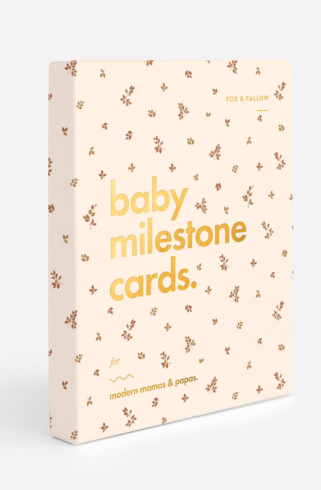 A beige box with small brown floral patterns featuring the text "Baby Milestone Cards Broderie" in large, gold letters on the front, and "for modern mamas & papas." in smaller, brown font beneath it. Perfect for commemorating important milestones, the brand "FOX & FALLOW" is printed in the top right corner.