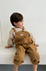Boy sitting on bench and smiling wearing the carpenter overalls